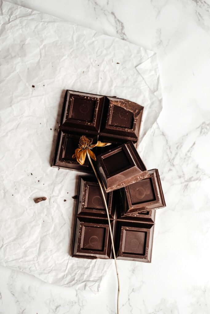 A flat lay of dark chocolate pieces with a dried flower elegantly placed, emphasizing artisanal confectionery.