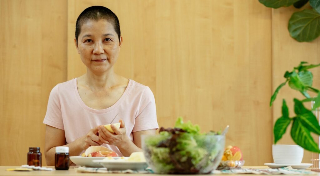 Asian woman with short hair prepares a healthy breakfast, surrounded by fruits and greens.