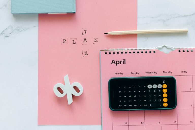 Flat lay of April calendar with calculator, pencil, and pink background for financial planning.