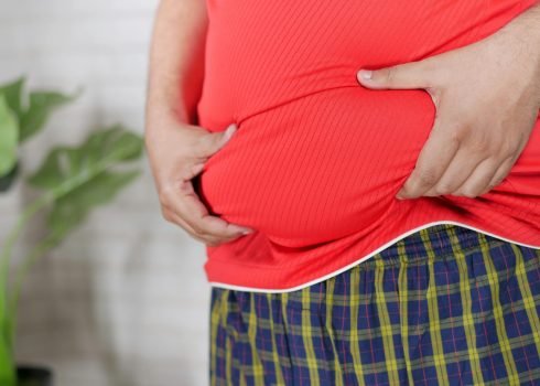 A man in a red shirt holding his midsection, focusing on health issues.