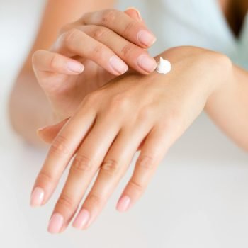 A woman applying cream on her hands, highlighting skincare and self-care concepts.