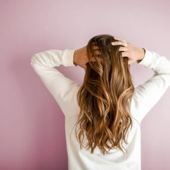 Back view of a woman with elegant long brown hair against a pink wall, showcasing stylish hair design.